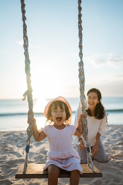 Niña feliz y madre balanceándose en la playa