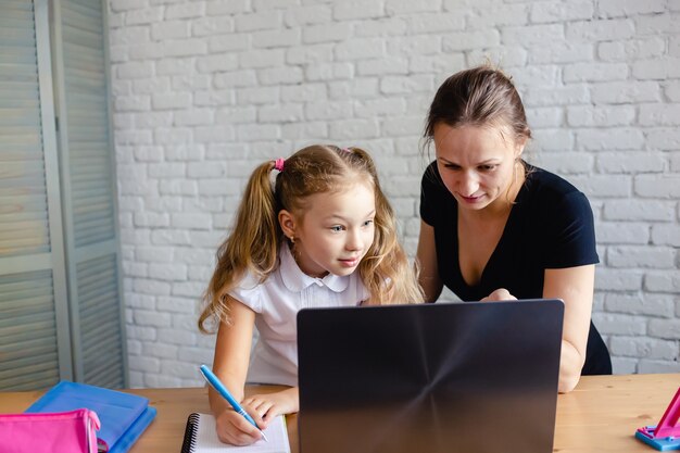 Niña feliz con madre estudiando en línea en casa. Virus corona y concepto de cuarentena.