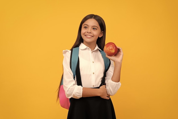 Niña feliz mantenga manzana y mochila escolar conocimiento de fondo amarillo