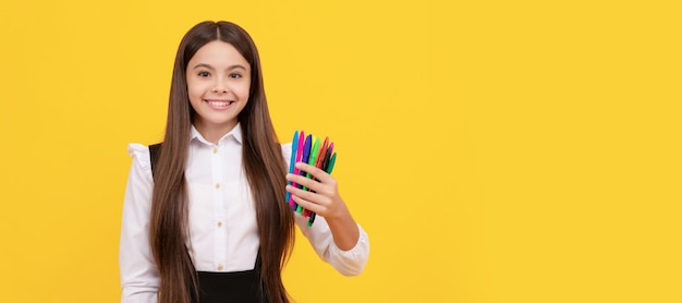 Niña feliz mantenga papelería escolar fondo amarillo rotuladores Banner de colegiala estudiante Retrato de alumno de niño de escuela con espacio de copia