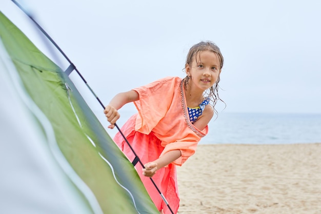Una niña feliz mira desde una tienda de campaña a la orilla del mar