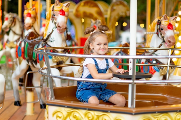 Niña feliz montando en carrusel en un parque de atracciones