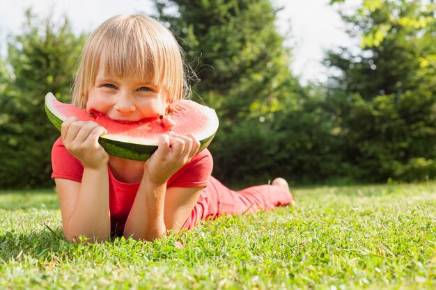 Niña feliz mordiendo una rebanada de melón en un jardín de verano