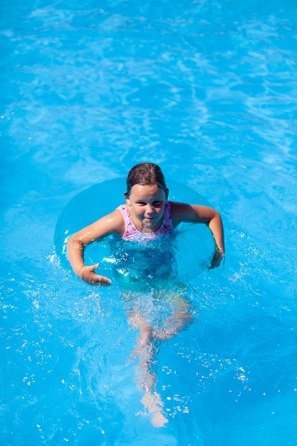 Una niña feliz nada en una piscina en un círculo inflable para mayor seguridad en el agua con espacio de copia