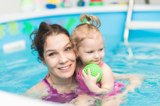 Niña feliz nada en la piscina con su madre