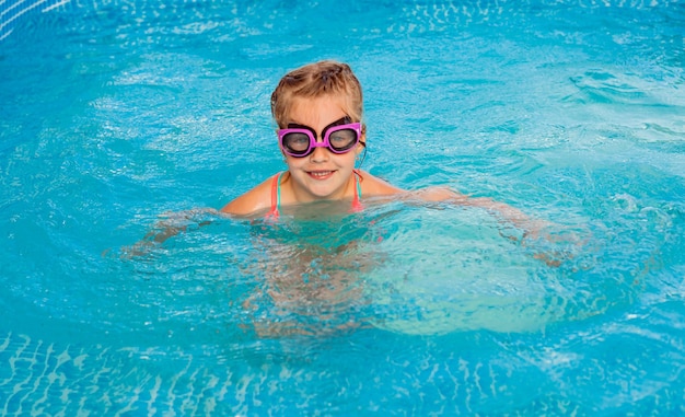 Niña feliz nada en la piscina. vacaciones de verano. chica en traje de baño y gafas de natación.