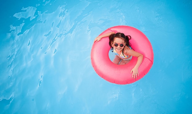 Niña feliz nadando en la piscina en un anillo inflable