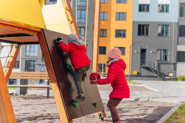 Niña feliz y niño jugando en la diapositiva niña en el patio de recreo