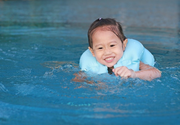 La niña feliz del niño nada en piscina lleva un salvavidas