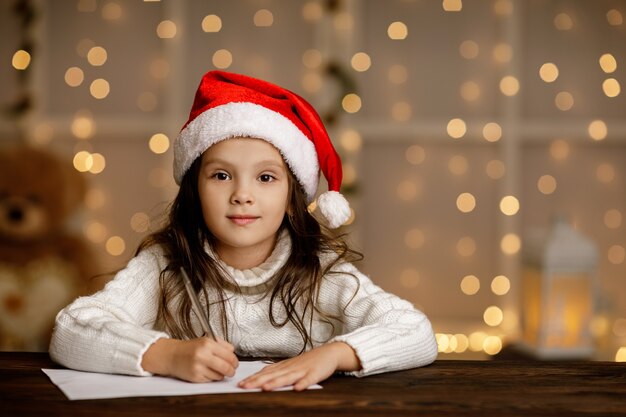 Niña feliz niño con sombrero de santa escribiendo lista de deseos o carta a Santa Claus