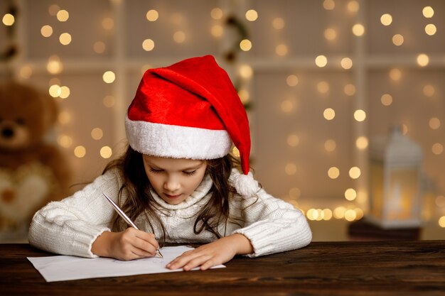 Niña feliz niño con sombrero de santa escribiendo lista de deseos o carta a Santa Claus