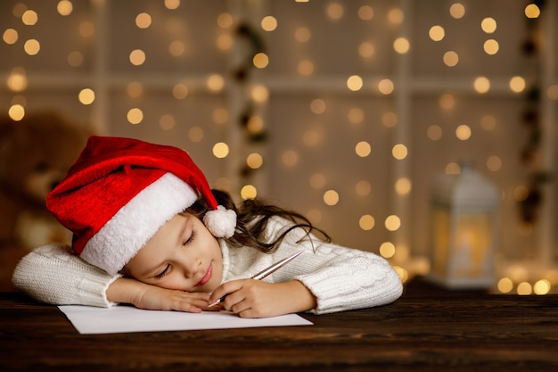 Niña feliz niño con sombrero de santa escribiendo lista de deseos o carta a Santa Claus