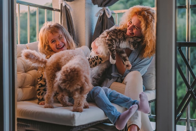 Una niña feliz, un niño con una sonrisa, juega en una vernada de primavera de verano en casa con mamá y un perro