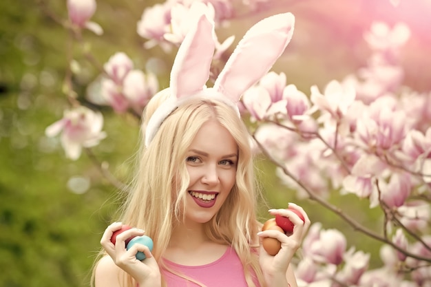 Niña feliz o linda mujer con huevos de pascua, orejas de conejo en magnolia floreciente. Primavera. Pascua de Resurrección. Fiestas, celebración.