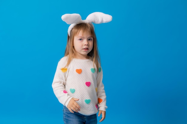 Una niña feliz con orejas de conejo en la cabeza y una caja de regalo sobre un fondo azul Espacio conceptual de Pascua para texto