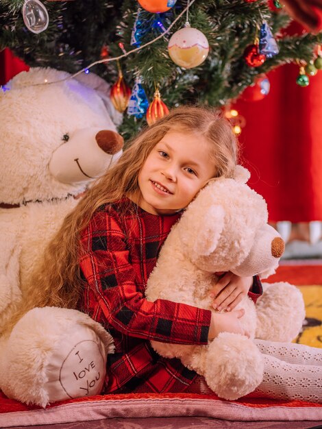 Niña feliz con un oso cerca del árbol de Navidad