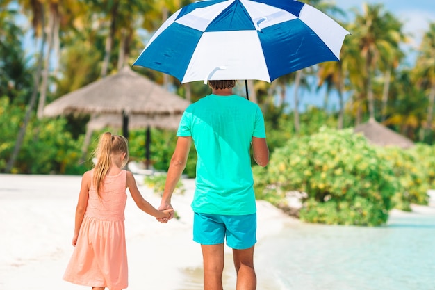 Niña y feliz papá caminando por la playa con un paraguas