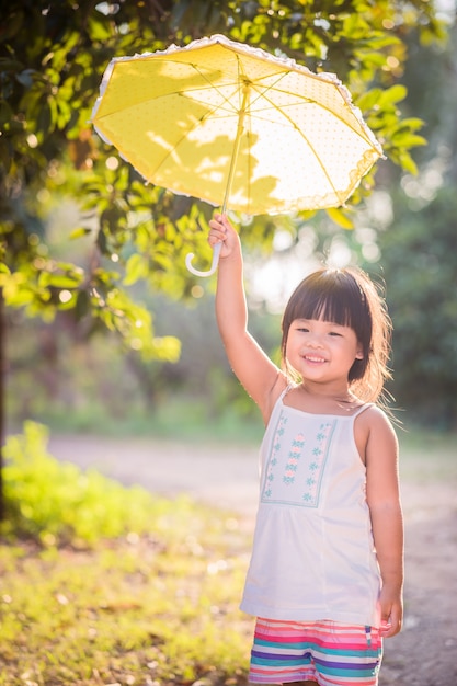 Niña feliz con paraguas caminando en el parque en un día soleado