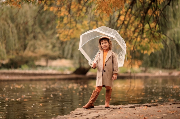 niña feliz con un paraguas transparente en un paseo en el otoño por el lago