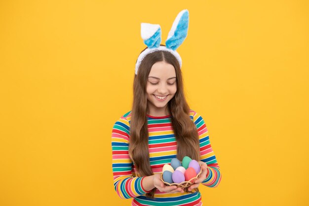 Niña feliz pascua en orejas de conejo sostiene huevos coloridos para el conejito de pascua de vacaciones