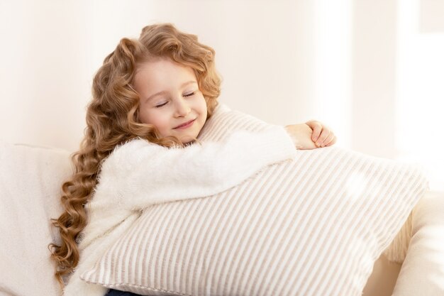 Niña feliz con el pelo largo abrazando una almohada y sonriendo