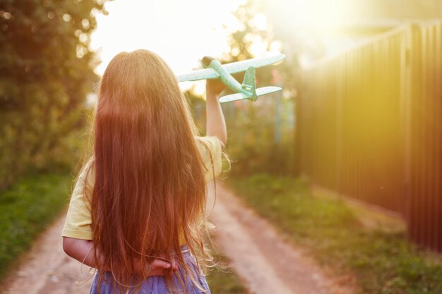 Niña feliz con el pelo largo y rubio jugando con un avión de juguete al aire libre al atardecer