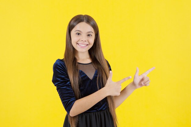 Niña feliz con el pelo largo sobre fondo amarillo dedo acusador en el espacio de la copia, publicidad.