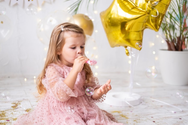 Niña feliz con el pelo largo en vestido rosa soplando silbato y celebrando su cumpleaños