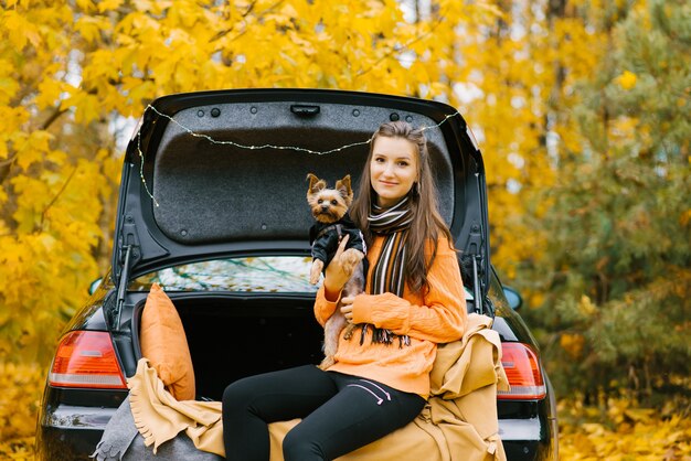 Niña feliz y perro sentado en el maletero de un coche en la naturaleza.