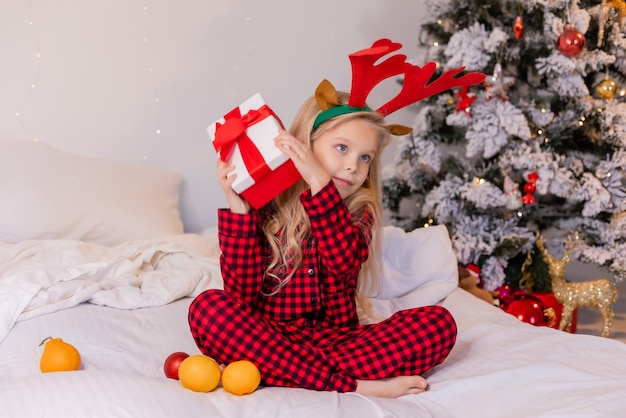 niña feliz en pijama en casa se regocija y desempaca regalos para Navidad. foto de alta calidad