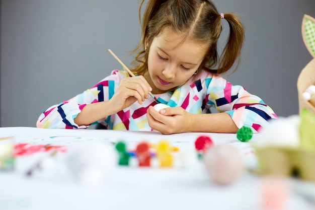 Niña feliz pintando, dibujando con huevos de pincel en casa. Niño preparándose para la Pascua, divirtiéndose y celebrando la fiesta. Felices Pascuas, DIY