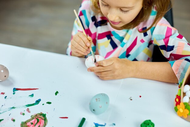 Niña feliz pintando dibujo con huevos de pincel en casa Niño preparándose para la Pascua divirtiéndose y celebrando la fiesta Feliz Pascua DIY