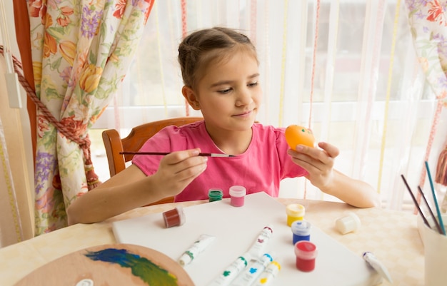 Niña feliz pintando huevos de Pascua en la mesa de la cocina