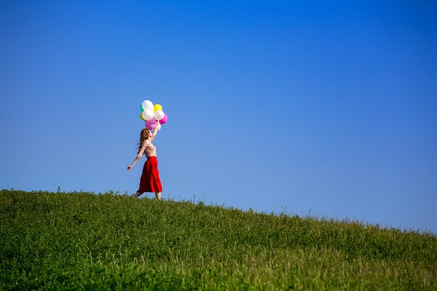 Niña feliz en los prados de la Toscana con globos de colores, contra el cielo azul y el prado verde. Toscana, Italia