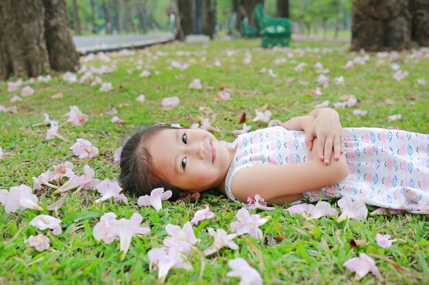 Niña feliz que miente en hierba verde con la flor del rosa de la caída en el jardín al aire libre.