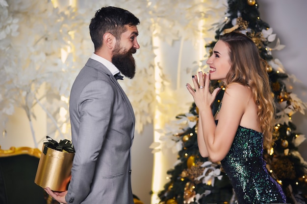 Niña feliz se regocija con el regalo con arco en la sala festiva cerca del árbol de navidad