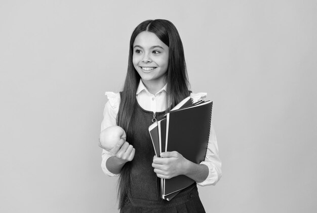 Niña feliz de regreso a la escuela con manzana y libros día de conocimiento de fondo amarillo