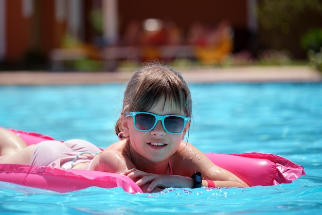 Niña feliz relajándose en un colchón de aire inflable en la piscina en un día soleado de verano durante las vacaciones tropicales Concepto de actividades de verano