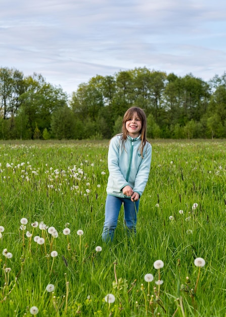 Una niña feliz se ríe alegremente y se para en un campo verde con diente de león esponjoso recogiendo alegremente la espuma de las flores Niños y naturaleza diversión de la infancia