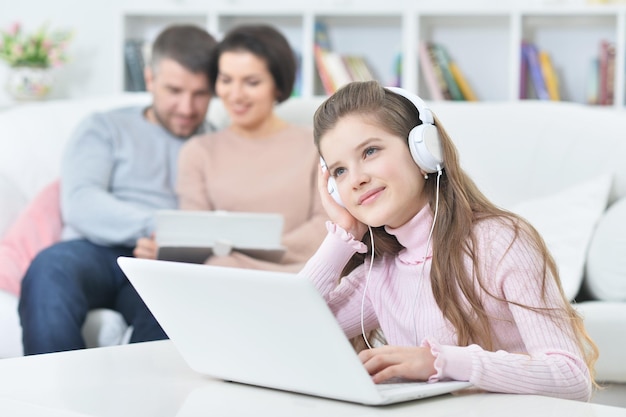 Niña feliz sentada en la mesa con una laptop con sus padres en el fondo