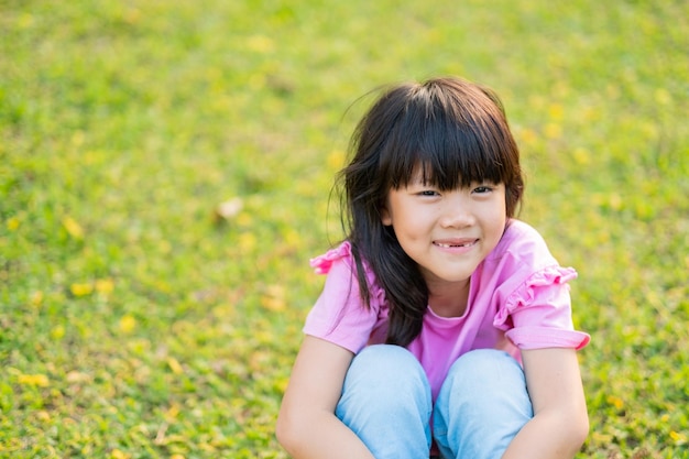 Niña feliz sentada en el patio de juegos de hierba