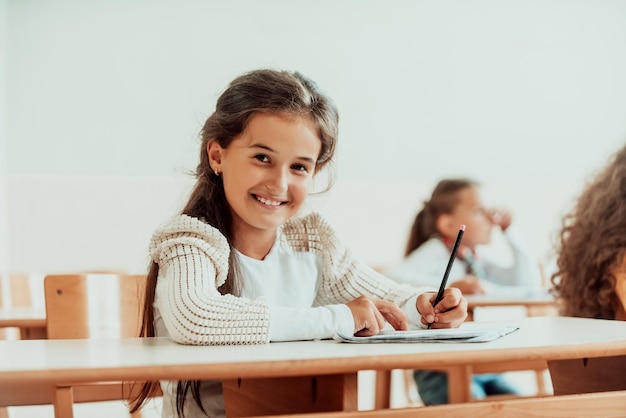 Una niña feliz sentada en un pupitre escolar y escribe en su cuaderno Enfoque selectivo Foto de alta calidad