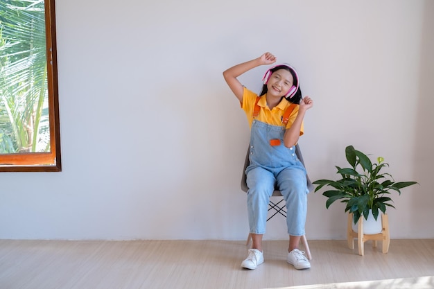 La niña feliz sentada en una silla escuchando música en una habitación mínima en casa