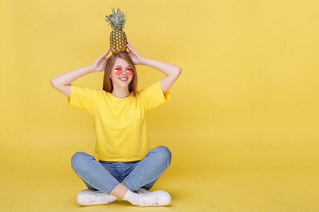 Niña feliz sentada en vasos y con piña en la pared de verano brillante