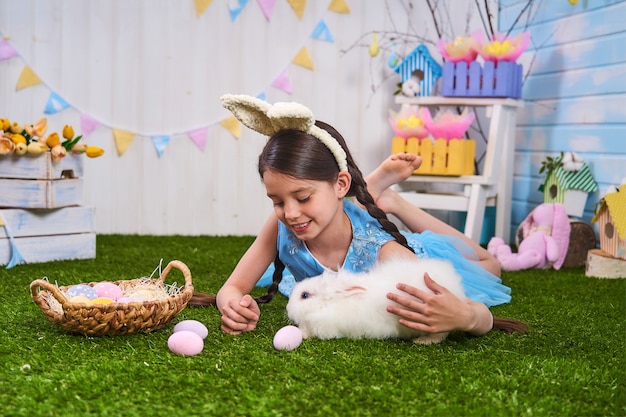 Niña feliz se sienta en el césped con huevos pintados y alimenta a las mascotas conejo, el día de Pascua