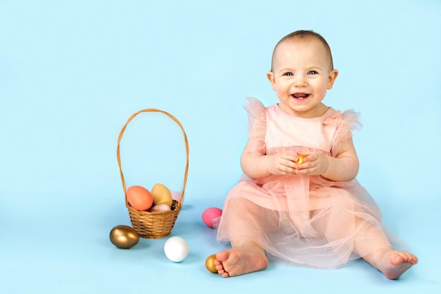 Niña feliz sobre fondo azul de estudio y jugando con huevos de Pascua de colores