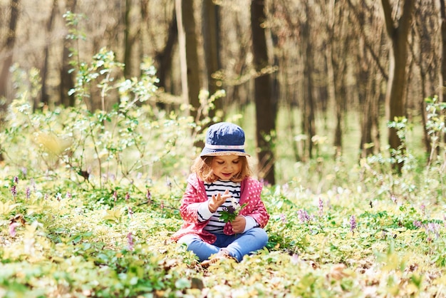 Una niña feliz con sombrero azul camina por el bosque de primavera durante el día