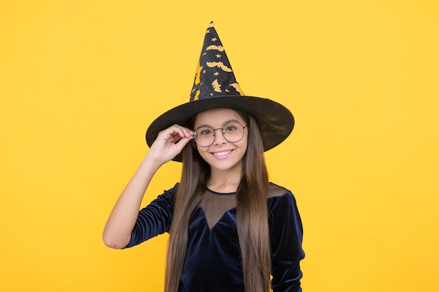 Niña feliz con sombrero de bruja y gafas listas para el encantamiento en halloween feliz halloween