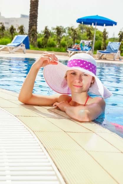 Niña feliz con un sombrero junto a la piscina en el mar