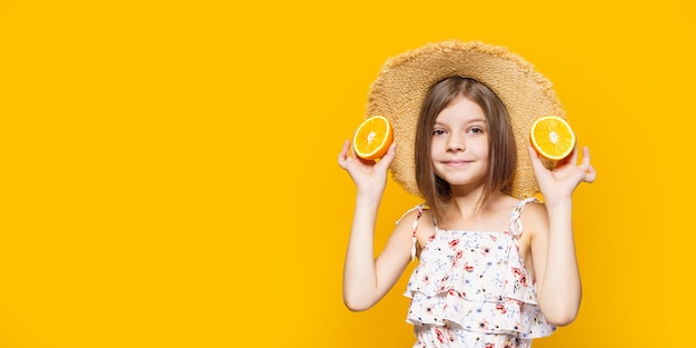 Niña feliz con un sombrero de paja sosteniendo una naranja sobre un fondo amarillo con espacio para texto